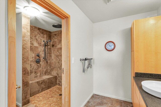 full bathroom featuring a tile shower, baseboards, and vanity