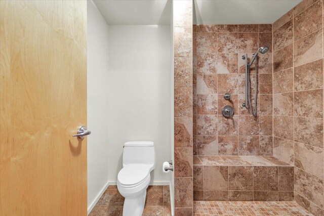 full bathroom featuring a tile shower, toilet, and tile patterned flooring