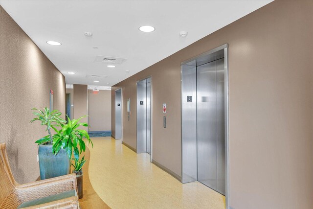 hallway featuring elevator, recessed lighting, light flooring, and baseboards