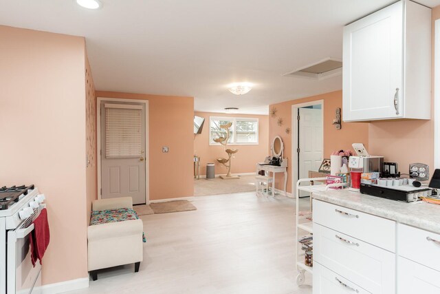kitchen featuring baseboards, gas range gas stove, light wood-style floors, light countertops, and white cabinetry