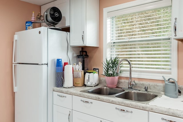 kitchen with a sink, light countertops, white cabinets, and freestanding refrigerator