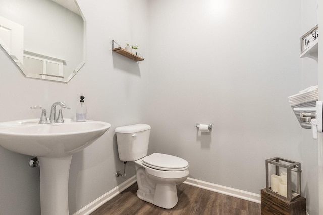 half bathroom with toilet, wood finished floors, baseboards, and a sink