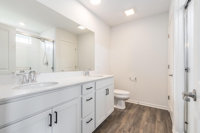 bathroom with a stall shower, wood finished floors, baseboards, double vanity, and toilet
