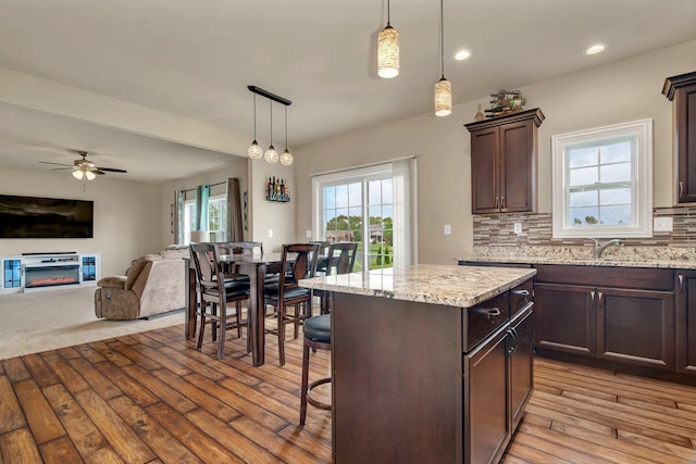 kitchen featuring decorative backsplash, dark brown cabinetry, open floor plan, ceiling fan, and light wood-style flooring