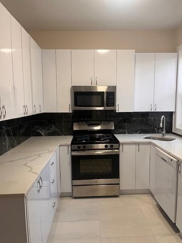 kitchen featuring decorative backsplash, light stone countertops, a sink, white cabinets, and stainless steel appliances