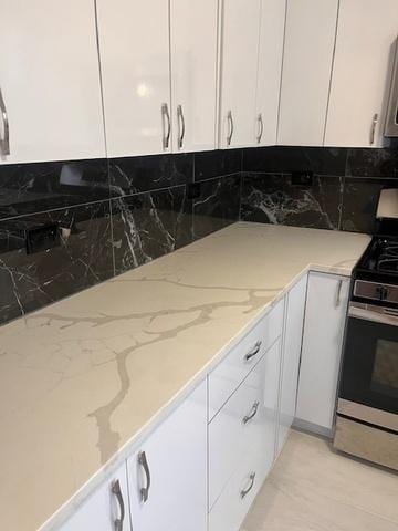 kitchen featuring light stone counters, tasteful backsplash, stainless steel gas stove, and white cabinets