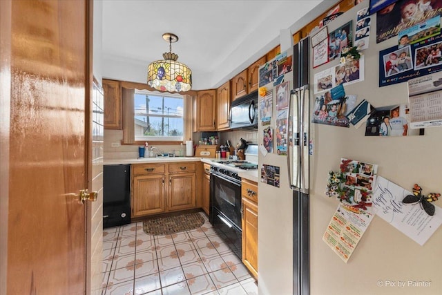kitchen featuring light countertops, brown cabinets, a sink, black appliances, and hanging light fixtures