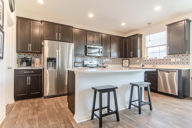 kitchen featuring decorative backsplash, dark brown cabinets, light countertops, stainless steel appliances, and light wood-style flooring