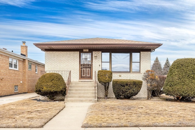 bungalow featuring brick siding and a shingled roof