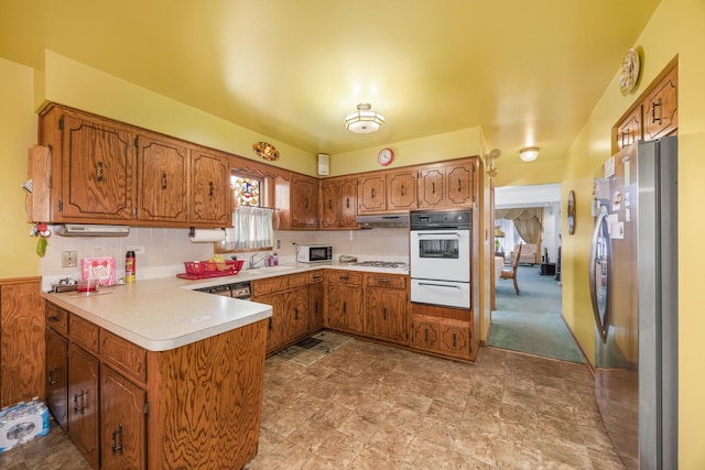 kitchen featuring brown cabinetry, a peninsula, a warming drawer, and white appliances