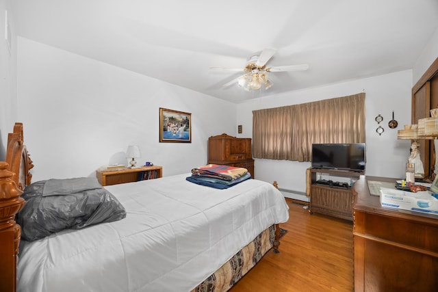 bedroom featuring ceiling fan, a baseboard heating unit, and wood finished floors