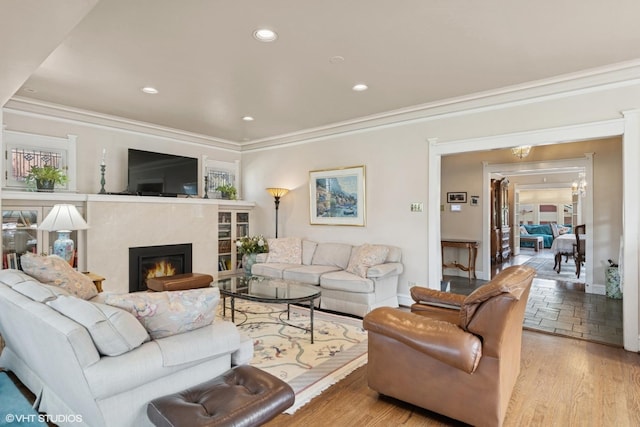 living area featuring wood finished floors, baseboards, a warm lit fireplace, ornamental molding, and recessed lighting