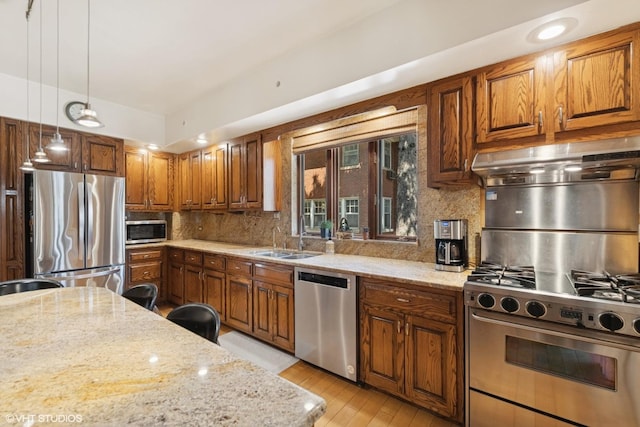 kitchen with light stone countertops, a sink, light wood-style floors, stainless steel appliances, and backsplash