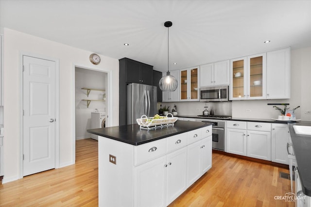 kitchen featuring stainless steel appliances, dark countertops, light wood finished floors, white cabinets, and a center island