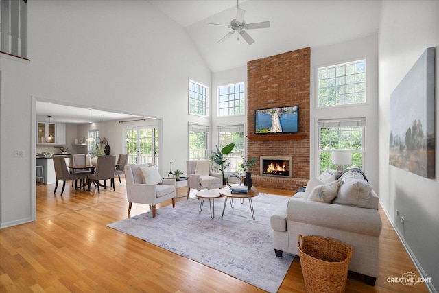 living room featuring high vaulted ceiling, a brick fireplace, ceiling fan, wood finished floors, and baseboards
