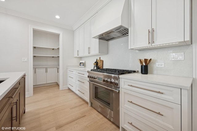 kitchen featuring light countertops, stainless steel range, white cabinets, light wood finished floors, and custom range hood