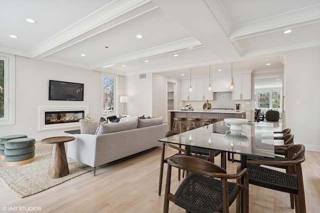 living area with recessed lighting, light wood-style flooring, a glass covered fireplace, and beam ceiling