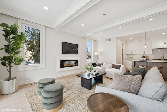 living room featuring visible vents, a glass covered fireplace, beam ceiling, and light wood-type flooring