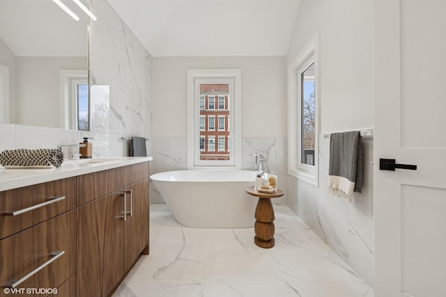full bathroom featuring wainscoting, vanity, marble finish floor, tile walls, and a soaking tub