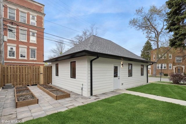 back of property with a lawn, fence, a garden, and roof with shingles