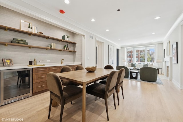 dining space with beverage cooler, light wood-type flooring, crown molding, and indoor wet bar