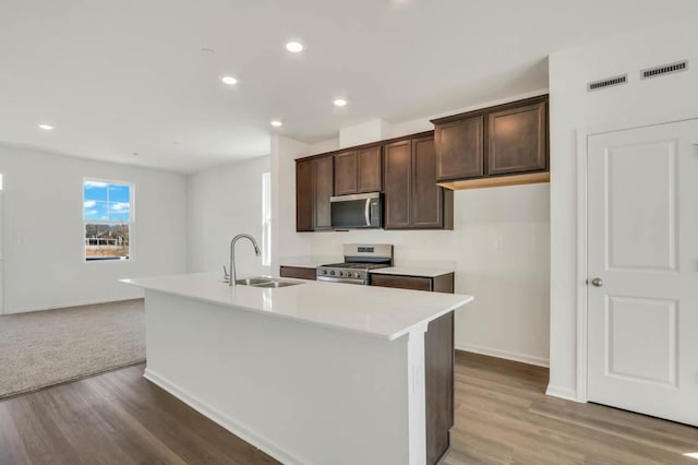 kitchen with dark brown cabinetry, appliances with stainless steel finishes, a sink, light wood-style flooring, and visible vents