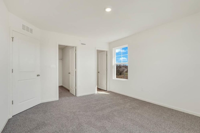 unfurnished bedroom with carpet floors, visible vents, baseboards, a walk in closet, and recessed lighting