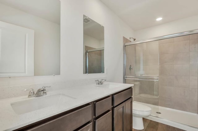 bathroom featuring a sink, a shower stall, toilet, and double vanity