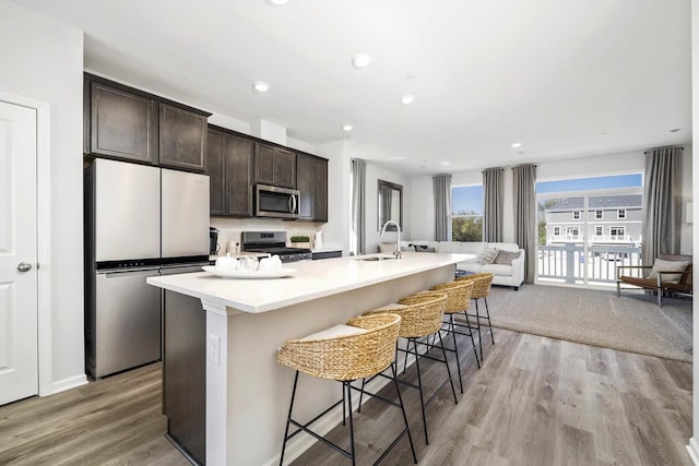 kitchen featuring dark brown cabinets, a kitchen breakfast bar, a center island with sink, a sink, and appliances with stainless steel finishes
