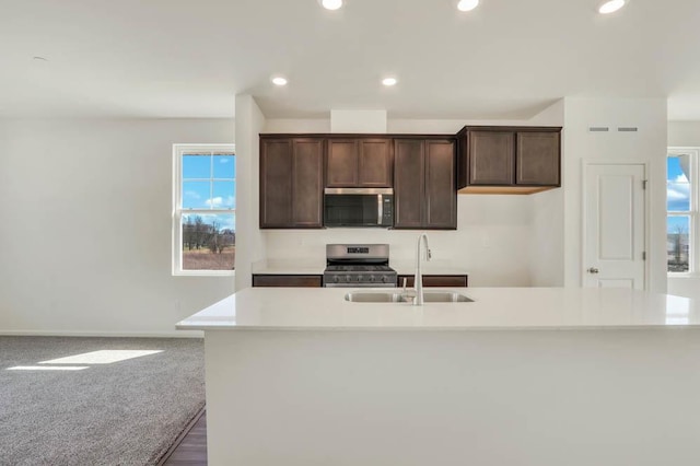 kitchen with a kitchen island with sink, appliances with stainless steel finishes, dark brown cabinets, a sink, and light countertops