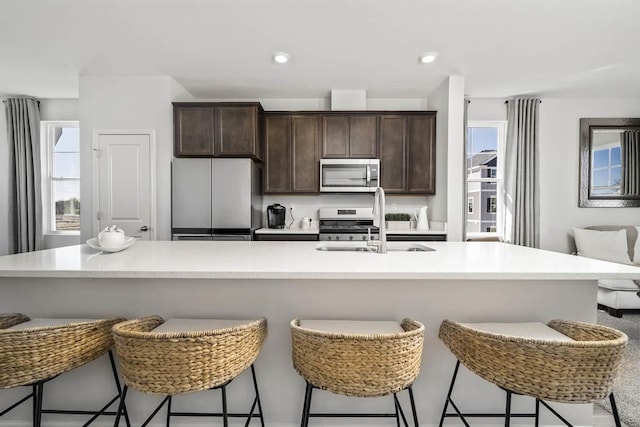 kitchen with light countertops, stainless steel appliances, a sink, and dark brown cabinets