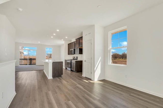 kitchen with wood finished floors, dark brown cabinetry, open floor plan, a center island with sink, and stainless steel appliances