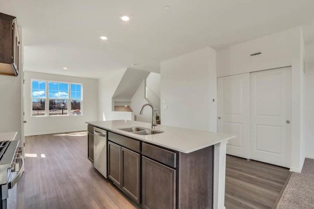 kitchen featuring wood finished floors, dark brown cabinetry, an island with sink, a sink, and stainless steel appliances