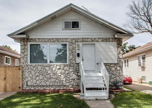 bungalow-style house with fence, stone siding, and cooling unit