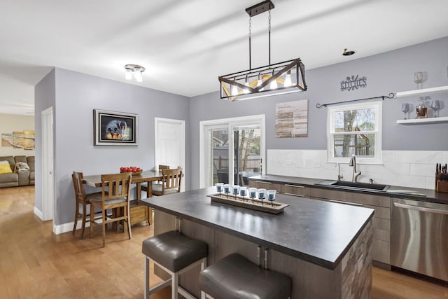 kitchen with light wood-style floors, a sink, dishwasher, and dark countertops