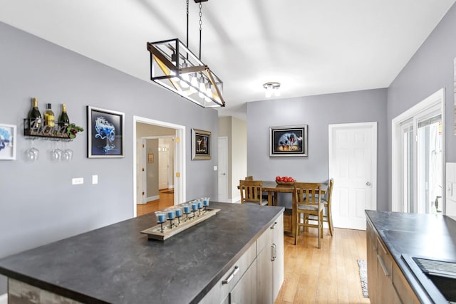 kitchen with pendant lighting, light wood finished floors, a kitchen island, and dark countertops
