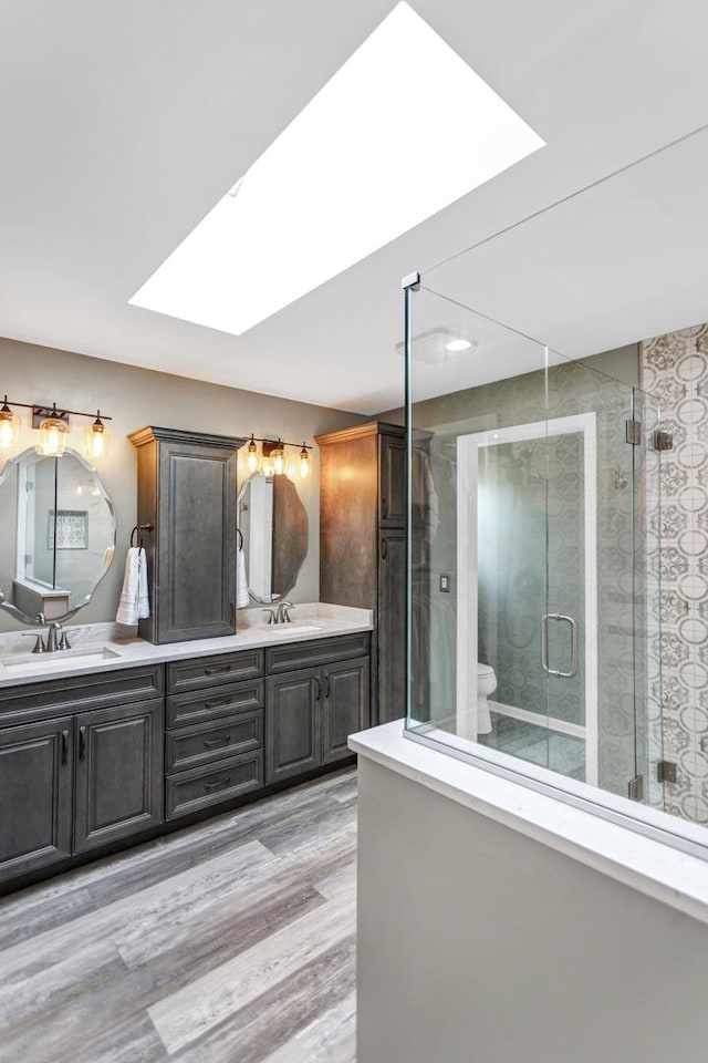 bathroom featuring double vanity, a skylight, a stall shower, a sink, and toilet