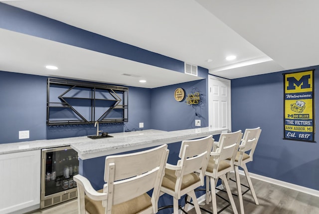 bar featuring visible vents, baseboards, a bar, wine cooler, and light wood-style flooring
