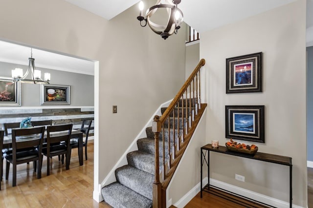 stairway with baseboards, a notable chandelier, and wood finished floors