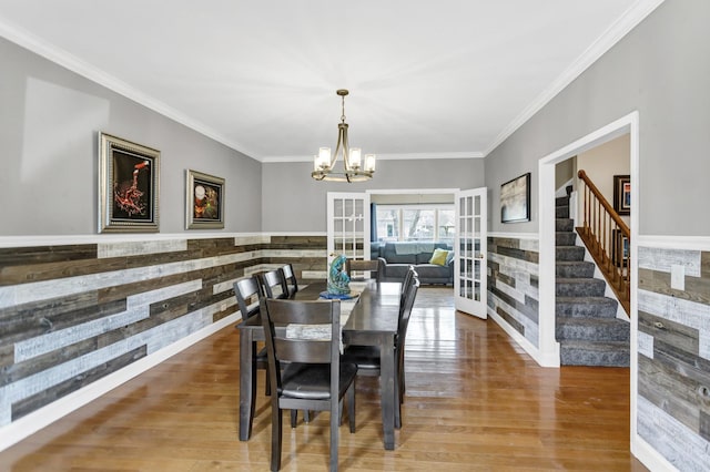 dining room with an inviting chandelier, french doors, wood finished floors, ornamental molding, and stairway