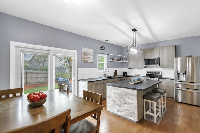 kitchen with dark countertops, appliances with stainless steel finishes, a center island, open shelves, and a sink