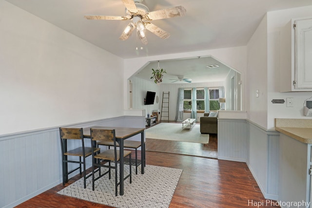 dining room with ceiling fan, visible vents, dark wood-style floors, and a wainscoted wall