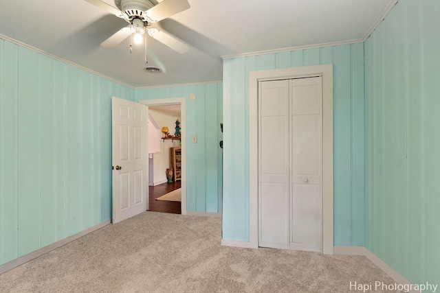 unfurnished bedroom featuring a ceiling fan, crown molding, baseboards, a closet, and carpet flooring