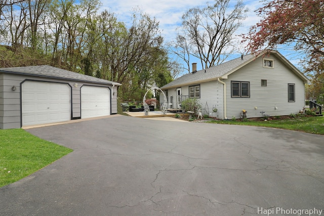exterior space with an outdoor structure, a shingled roof, a chimney, and a detached garage