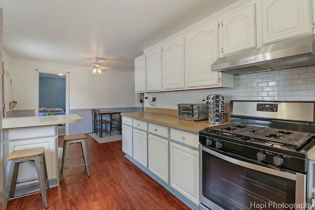 kitchen featuring ceiling fan, dark wood finished floors, gas stove, under cabinet range hood, and white cabinetry