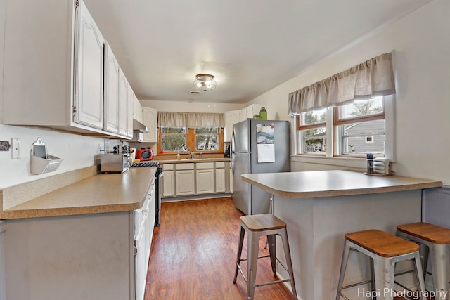 kitchen featuring dark wood-style flooring, a peninsula, a breakfast bar, a sink, and appliances with stainless steel finishes