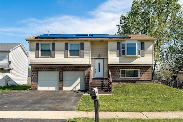 bi-level home with brick siding, asphalt driveway, an attached garage, and roof mounted solar panels