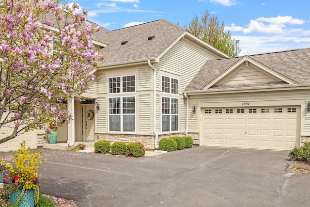 traditional-style house with a garage, a shingled roof, stone siding, and aphalt driveway
