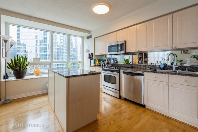 kitchen featuring light wood-style floors, a center island, a sink, dark stone countertops, and stainless steel appliances