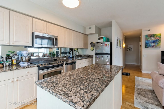 kitchen featuring light wood-style floors, stainless steel appliances, dark stone countertops, and open floor plan